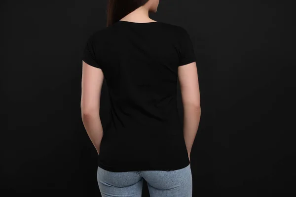 Woman wearing black t-shirt on dark background, back view