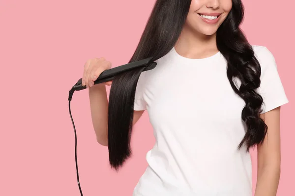 Happy woman using hair iron on pink background, closeup. Space for text
