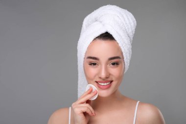 Havlu giymiş güzel bir kadın gri arka planda pamuklu ped ile makyajı temizliyor, mesaj için yer var.