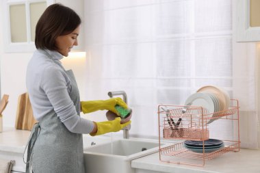 Modern mutfakta lavabonun üstünde genç ve mutlu bir kadın bulaşık yıkıyor.