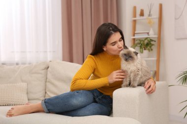 Evdeki rahat kanepede sevimli kedisini öpen bir kadın.