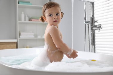 Şirin küçük kız evde köpüklü banyo yapıyor.
