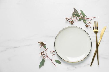 Çatal bıçak takımları ve okaliptüs yapraklarıyla beyaz mermer masa, düz. Metin için boşluk