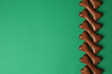 Bone shaped dog cookies on green background, flat lay. Space for text