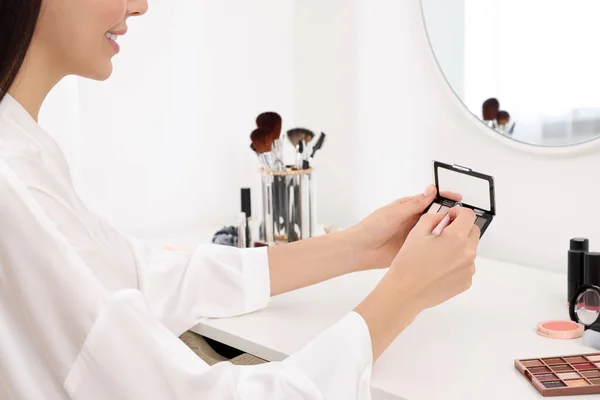 Woman with eyeshadow palette and brush at dressing table, closeup