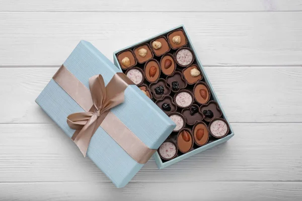 Open box of delicious chocolate candies on white wooden table, top view