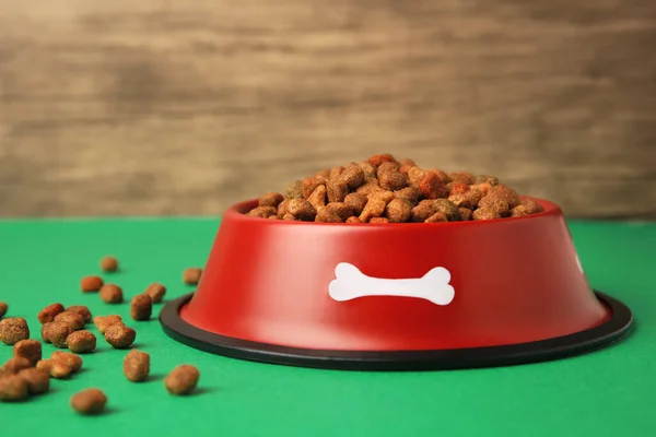 Dry pet food in feeding bowl on green background, closeup
