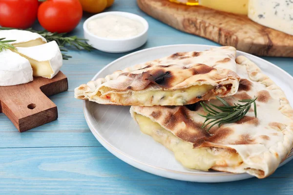 Peynirli lezzetli pizzalar ve açık mavi ahşap masa üzerinde farklı ürünler, yakın plan.