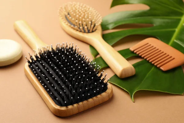 stock image Wooden hairbrushes, comb, solid shampoo and green leaf on light brown background