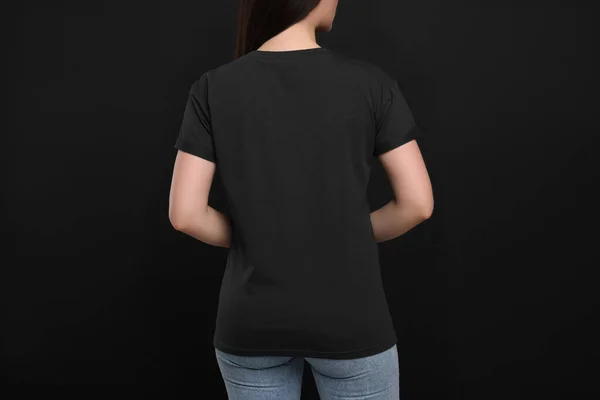 Woman wearing black t-shirt on dark background, back view