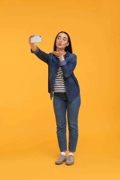 Jovem Mulher Tomando Selfie Com Smartphone Soprando Beijo Fundo Amarelo — Fotografia de Stock