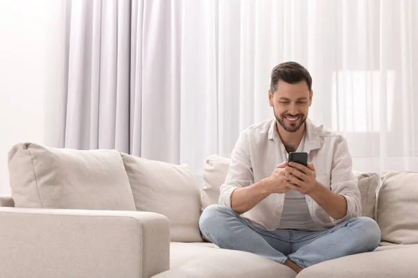 Mann Mit Smartphone Auf Sofa Neben Fenster Mit Schönen Vorhängen — Stockfoto