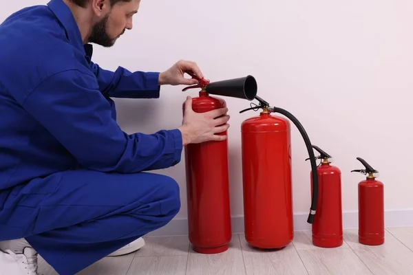 stock image Man in uniform checking fire extinguishers indoors