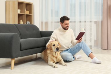 Adam yerde kitap okuyor. Evindeki şirin Labrador Retriever 'ının yanında.