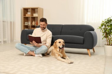 Adam yerde kitap okuyor. Evindeki şirin Labrador Retriever 'ının yanında.