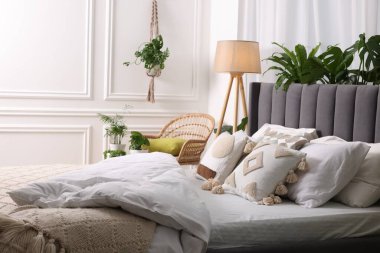 Yatak odasında büyük, rahat bir yatak, lamba ve güzel bitkiler. İç tasarım