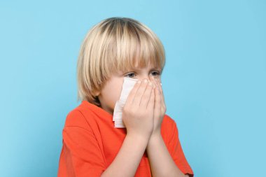 Açık mavi arka planda burnu dokuya sümküren çocuk. Soğuk belirtileri