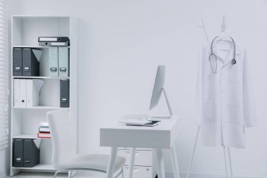 Klinikte askıda asılı duran beyaz doktor önlüğü ve steteskop.