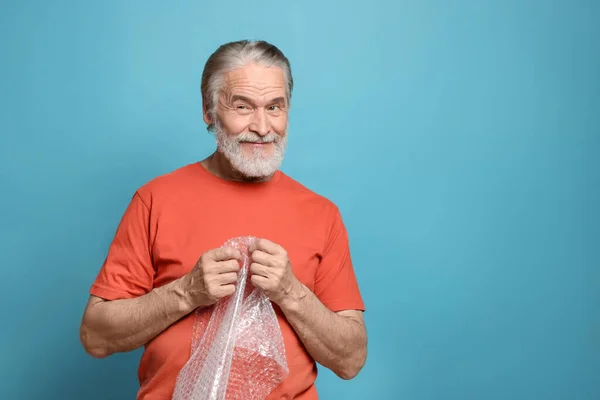 Happy Senior Man Popping Bubble Wrap Light Blue Background Space — Stock Photo, Image