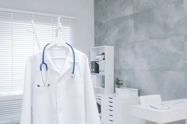 Λευκό Φόρεμα Γιατρού Και Στηθοσκόπιο Κρέμονται Στο Ράφι Στην Κλινική — Φωτογραφία Αρχείου