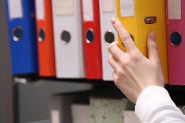 Woman taking folder with documents from shelf in office, closeup