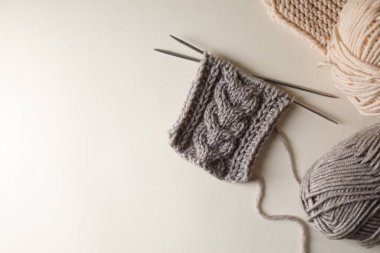 Örgü örme, bej arka planda yumuşak renkli iplikler ve iğneler, düz yatış. Metin için boşluk