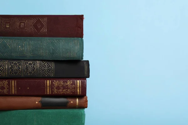 Stack of old books on light blue background, space for text