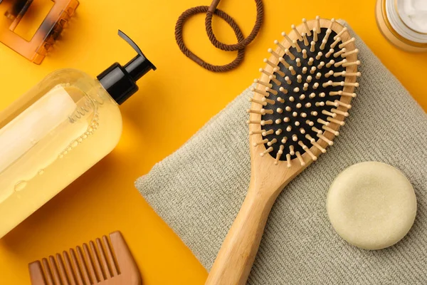 Wooden brush, comb and different hair products on orange background, flat lay