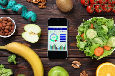 Ağırlık kaybı hesap makinesi uygulamalı akıllı telefon, mezura ve ahşap masa üzerinde farklı ürünler, düz konum