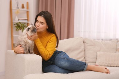 Evdeki rahat kanepede sevimli kedisini öpen bir kadın.