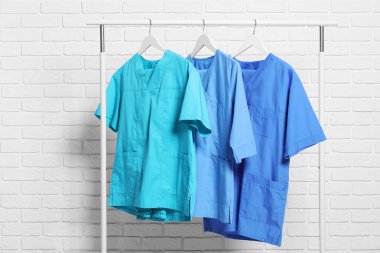 Medical uniforms hanging on rack near white brick wall clipart