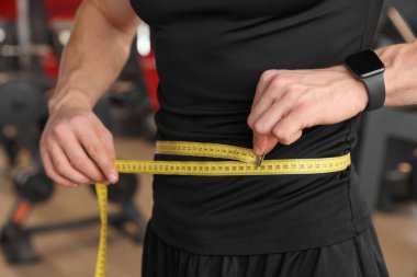 Spor salonunda belini bantla ölçen atletik adam, yakın plan.