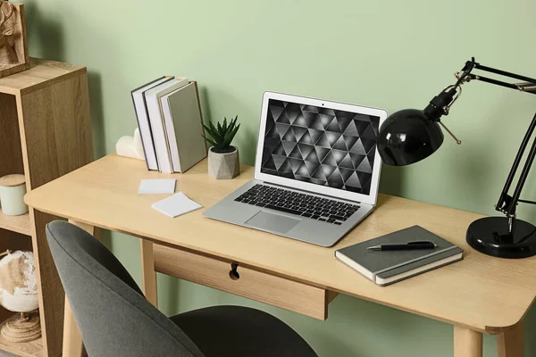 緑の壁の近くの木製の机の上にモダンなラップトップ ランプ 文房具 内務省 — ストック写真