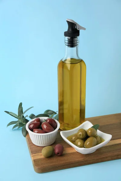 Bottle of oil, olives and tree twig on light blue background