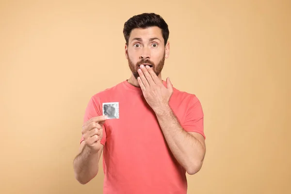 Emotional Man Holding Condom Beige Background Safe Sex — Stock Photo, Image