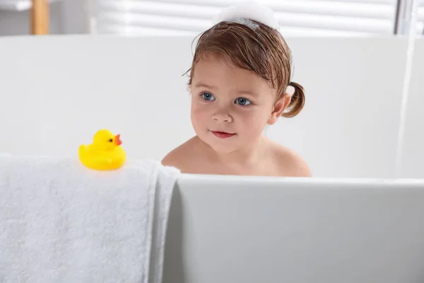 stock image Cute little girl taking bath with toy indoors