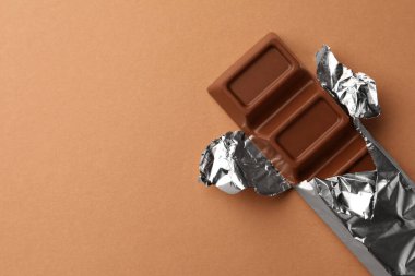 Açık kahverengi arka planda folyoya sarılı nefis çikolata, üst manzara. Metin için boşluk