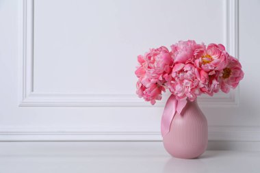 Beyaz duvarın yanındaki vazoda pembe şakayık demeti var. Metin için boşluk