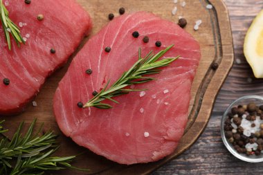 Raw tuna fillets with rosemary and peppercorns on wooden board, top view clipart