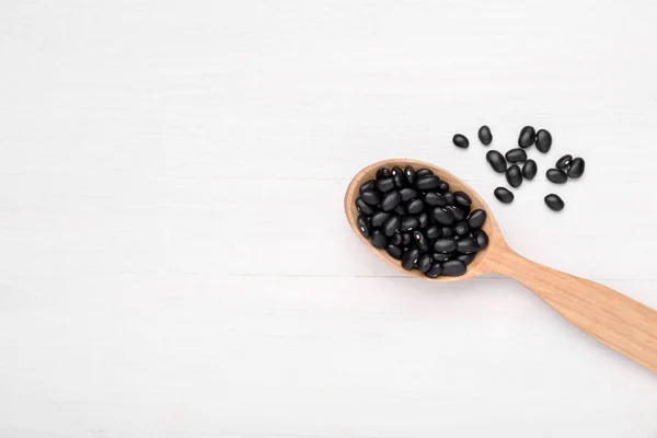 stock image Spoon of raw black beans on white wooden table, top view. Space for text