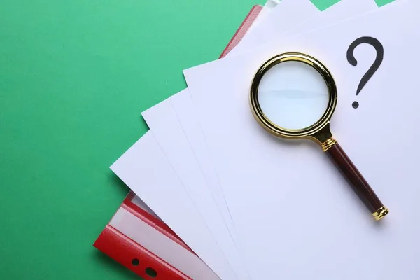 Magnifying glass, folder with paper sheets and question mark on green background, top view