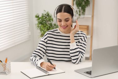 Çevrimiçi çeviri kursu. Kulaklık takan öğrenci evde dizüstü bilgisayarın yanında yazıyor.