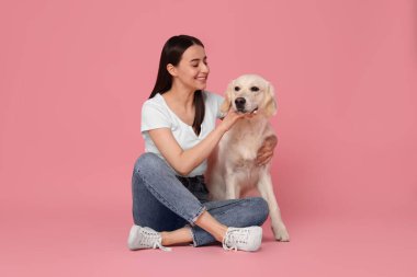 Pembe arka planda şirin Labrador Retriever köpeği olan mutlu bir kadın. Sevimli hayvan.