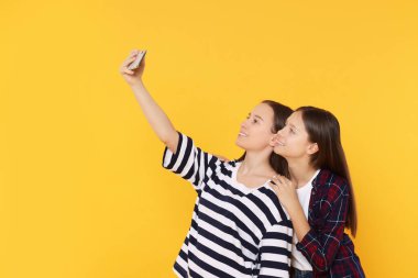 Turuncu arka planda selfie çeken genç kızlar.