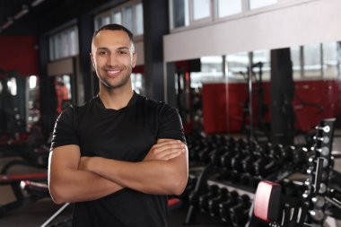 Happy trainer in modern gym, space for text