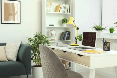 Modern dizüstü bilgisayarı beyaz ahşap masa ve evdeki rahat koltuğu olan rahat çalışma alanı.