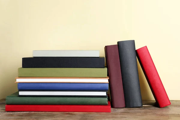 Many hardcover books on wooden table near yellow wall