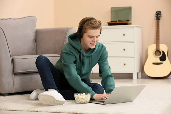 Stock image Teenage boy with headphones and popcorn using laptop at home