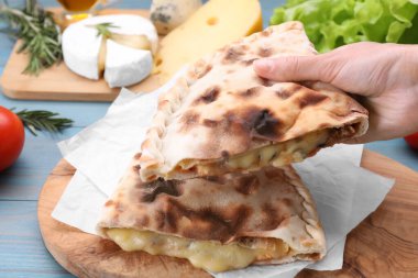 Açık mavi ahşap masada peynirli lezzetli pizzalı calzone tutan kadın, yakın plan.