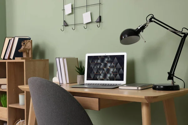 绿色墙壁附近木制书桌上的现代笔记本电脑 灯和文具 总部办公室 — 图库照片
